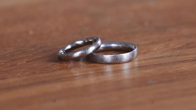 A pair of wedding rings lie on a wooden table. 